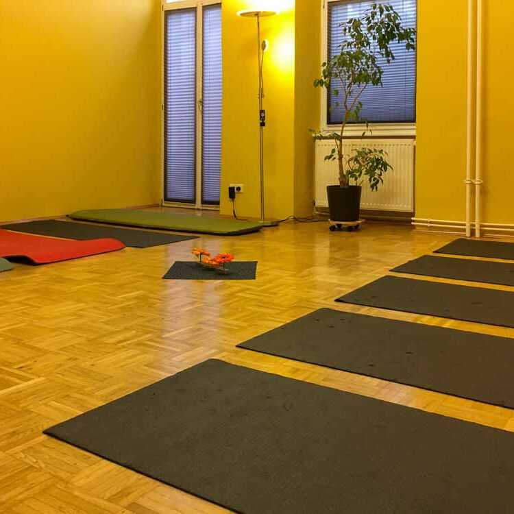 Der große Raum in der Coachingpraxis mit gelben Wänden, gedämpften Licht und zugezogenen Rollos. Auf dem Boden liegen Yoga-Matten.